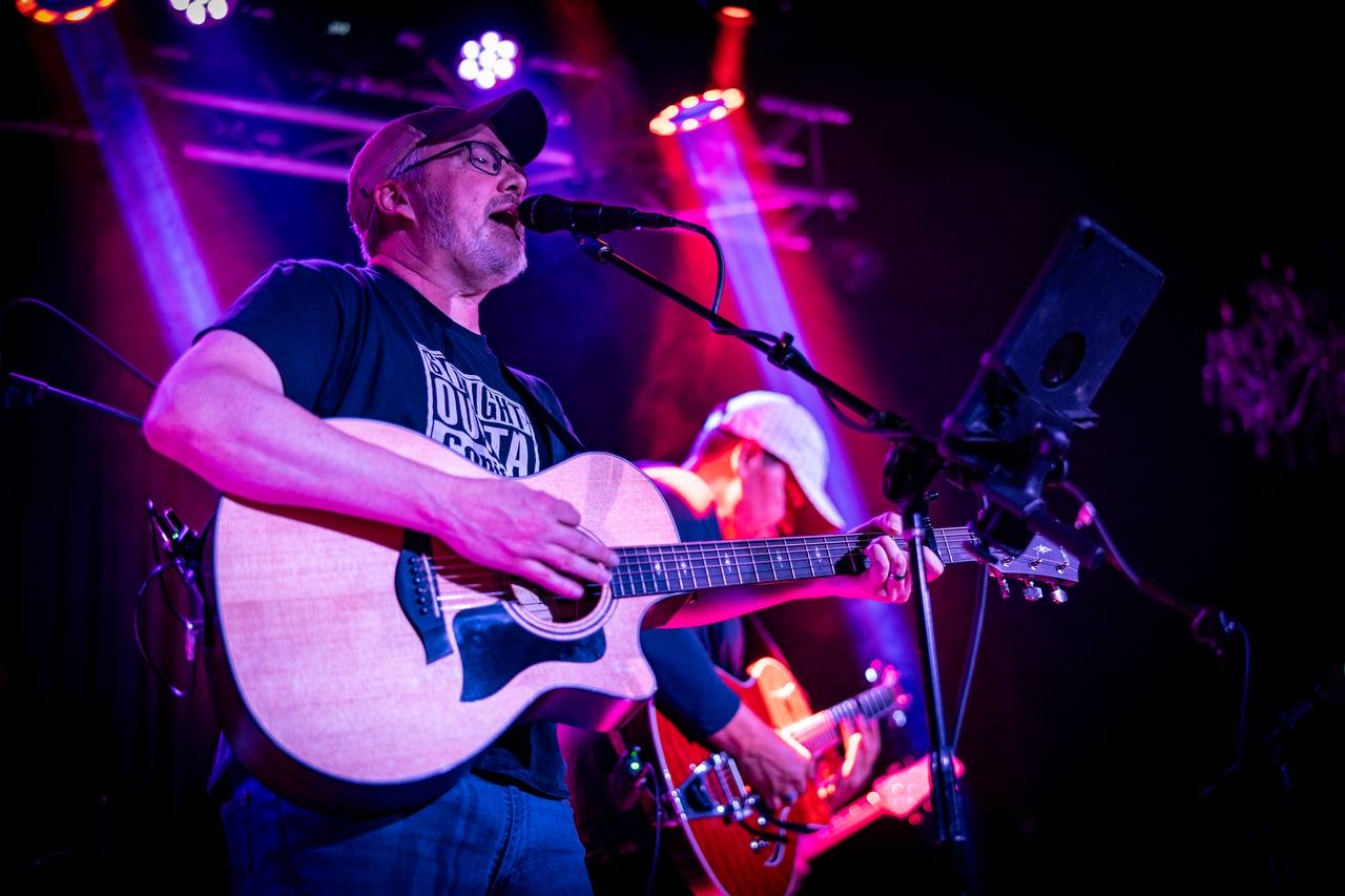 Lance singing with acoustic guitar under stage lights